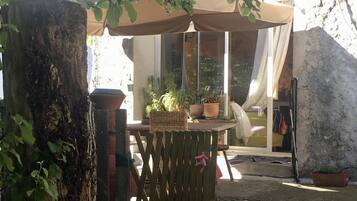 An outdoor patio area with a wooden table, potted plants, and a large tree trunk.