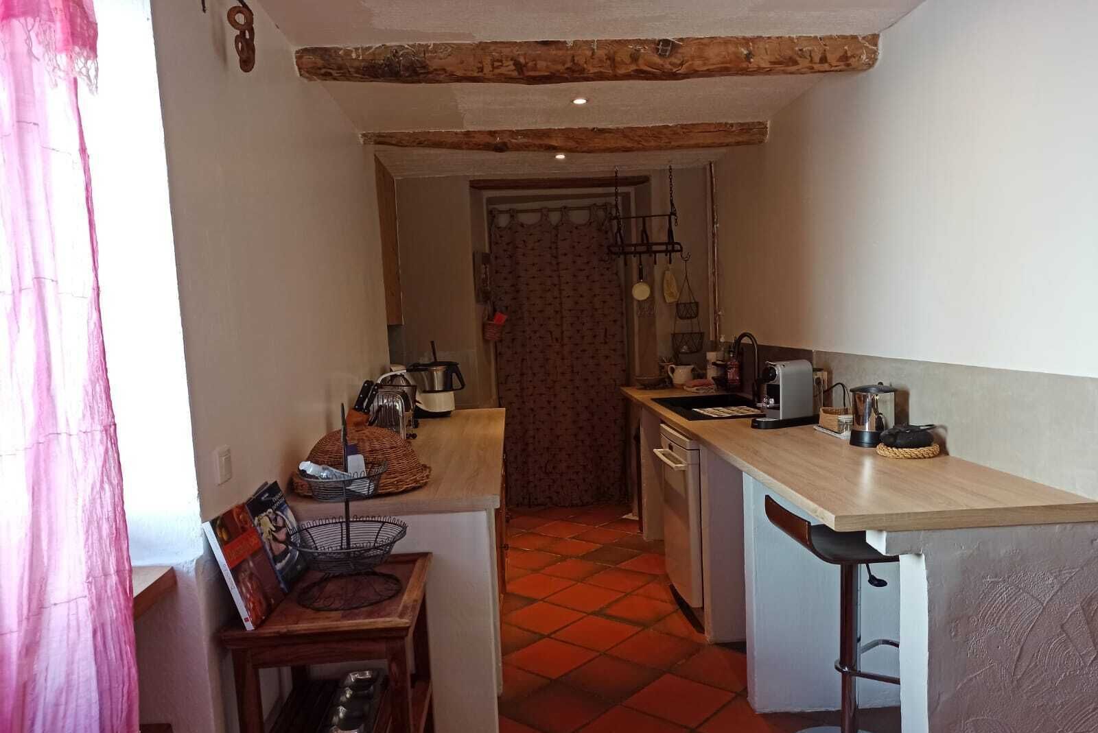 A compact kitchen with a wooden countertop, a sink, and a stove. There is a small dining area with a chair and a table.