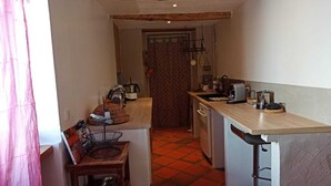 Eine kompakte Küche mit Holztischplatte, Spüle und Herd. Es gibt eine kleine Essecke mit einem Stuhl und einem Tisch.