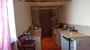 Una cucina compatta con un piano di lavoro in legno, un lavello e un fornello. È presente una piccola zona pranzo con una sedia e un tavolo.