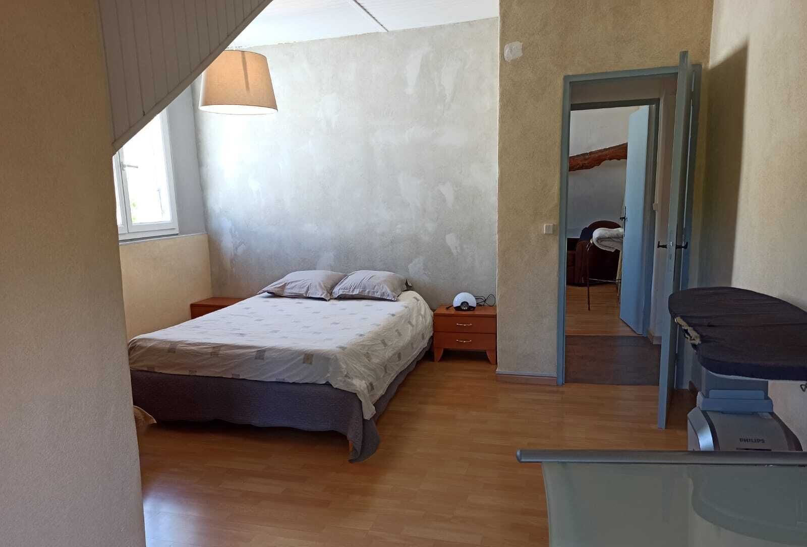 A bedroom with a bed, bedside table, lamp, and a desk with a chair.