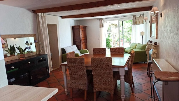Ein Essbereich mit einem Holztisch, Korbstühlen, einem grünen Sofa und einem Schrank mit Spiegel.