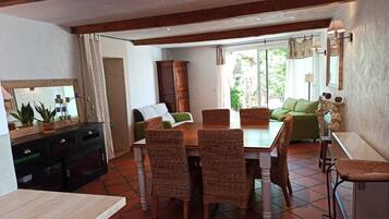 A dining area with a wooden table and wicker chairs, a green sofa, and a cabinet with a mirror.