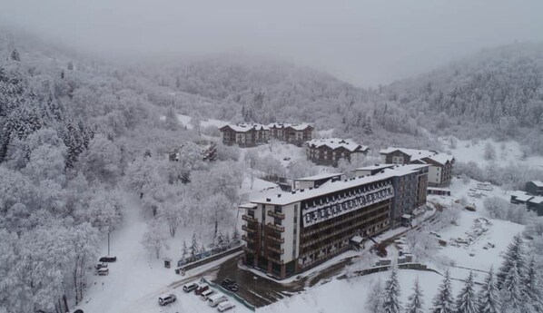 A multi-story hotel with a central courtyard, surrounded by snow-covered trees and hills.