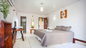 Une chambre à coucher comprenant un lit, un bureau en bois, un miroir et une porte donnant sur un balcon.