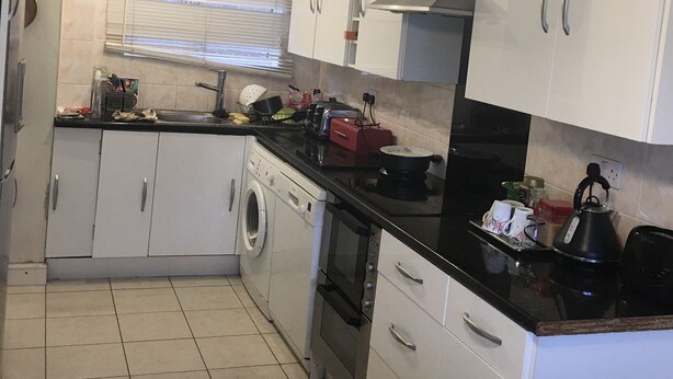 A compact kitchen with white cabinets, a washing machine, an oven, and a kettle. There are two pendant lights above the counter. - Sunny City (Peterborough)