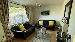 A living room with a black leather sofa, a glass coffee table, and a large window with curtains. - Sunny City (Peterborough)