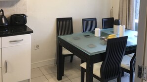 A dining area with a glass table, black chairs, a black toaster, and a painting of a tree-lined path on the wall. - Sunny City (Peterborough)