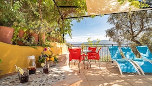 Une terrasse extérieure avec une table dressée pour deux personnes, des chaises rouges et bleues, et une vue sur les montagnes en arrière-plan.