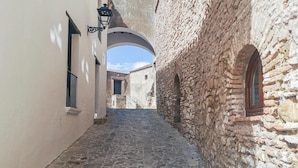 Une ruelle étroite pavée, bordée de bâtiments aux murs de pierre et à la façade blanche.