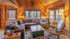 A cozy log cabin interior with a sectional sofa, a rocking chair, and a small table. - Cozy mountain cabin near Sugarloaf—your four‑season adventure escape (Eustis)
