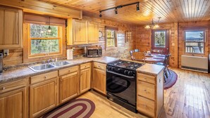 A wooden cabin kitchen with a stove, sink, microwave, and large windows. - Cozy mountain cabin near Sugarloaf—your four‑season adventure escape (Eustis)