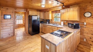 A wooden cabin kitchen with a central island, a refrigerator, a stove, a microwave, and wooden cabinets. - Cozy mountain cabin near Sugarloaf—your four‑season adventure escape (Eustis)