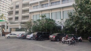 A parking lot with several cars and motorcycles, surrounded by multi-story buildings with balconies. - Hotel Stern Pattaya (Pattaya)