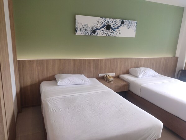A hotel room with two single beds, a wooden headboard, a telephone, and a floral artwork on the wall.