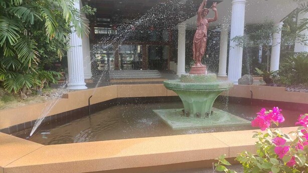 A fountain with water jets, surrounded by greenery and a statue. - Hotel Stern Pattaya (Pattaya)