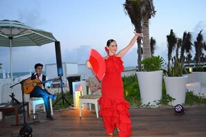 A person in a red dress dancing with a fan, a guitar player, and a beach setting with palm trees.