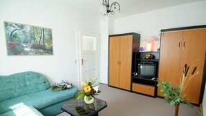 A living room with a teal sofa, a coffee table with a vase, a television on a wooden cabinet, and a door with a window.