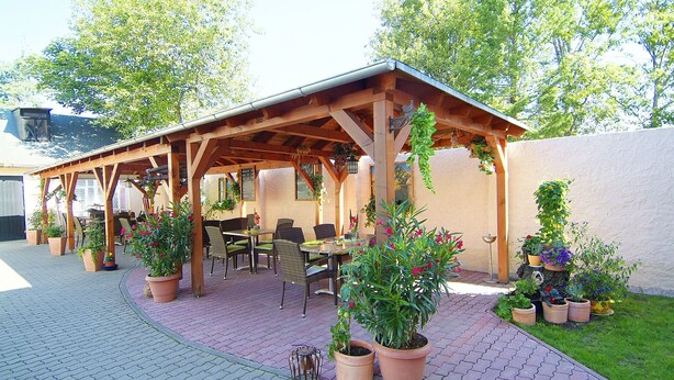 An outdoor patio area with a wooden pergola, potted plants, and outdoor seating.