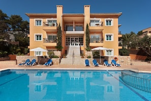 A multi-story hotel with a swimming pool, outdoor seating, and a staircase leading to the entrance.