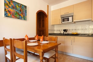 A dining table with chairs, a wooden door, and a kitchen with cabinets and a microwave.