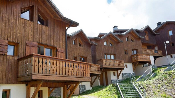Una hilera de edificios tipo chalet de madera con balcones y una escalera de piedra que lleva a la entrada.