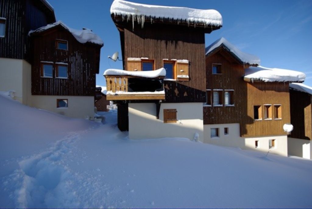 A snow-covered wooden chalet with multiple balconies and windows, surrounded by snow.