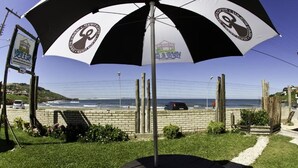 A beachside view with a black and white umbrella, a wooden deck, and a fence overlooking the ocean. - Pousada Vento & Cia (Laguna)