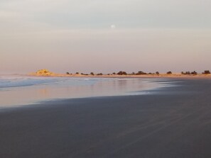 A beach with a calm sea, sandy shore, and sparse vegetation. - Pousada Vento & Cia (Laguna)