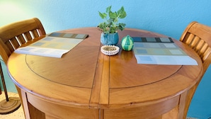 Una mesa redonda de madera con dos individuales, una planta en maceta, un objeto decorativo y un pequeño objeto verde.