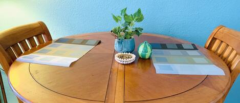 Una mesa redonda de madera con dos individuales, una planta en maceta, un objeto decorativo y un pequeño objeto verde.