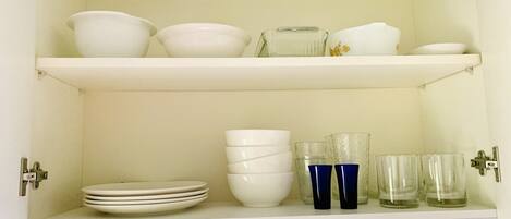 A white cabinet with shelves containing white bowls, plates, and glassware.