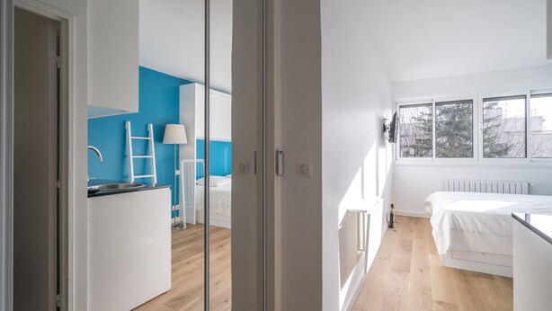 A modern bedroom with a large window, a white bed, and a wooden floor.