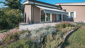 Une maison moderne dotée d’un patio couvert, de grandes fenêtres et d’un jardin bien entretenu.
