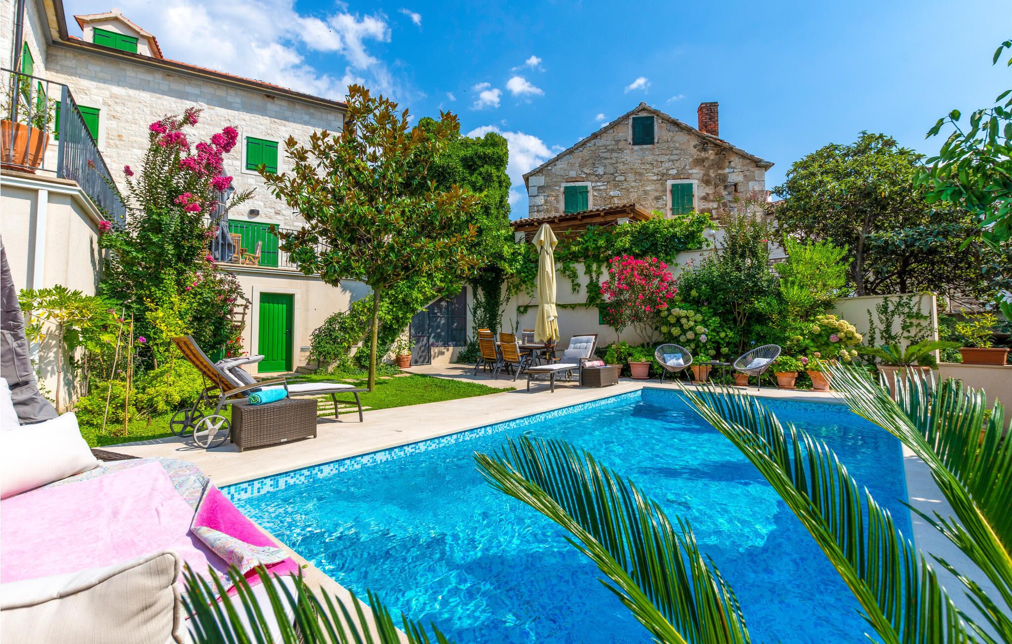 Ein Poolbereich mit Liegestühlen und ein Steinhaus mit grünen Fensterläden.