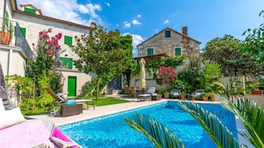 A pool area with lounge chairs and a stone building with green shutters. - Beautiful home in Postira (Postira)