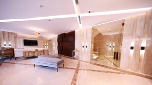 A spacious hotel lobby with a large seating area, a flat-screen TV mounted on the wall, and a staircase leading to an upper level. - EVA Hotel (Jeddah)