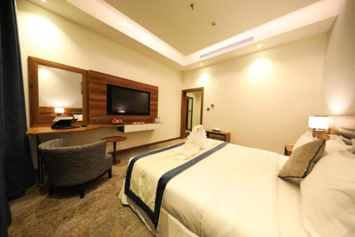 Une chambre d’hôtel avec un grand lit, un téléviseur fixé au mur, un bureau avec une chaise et une petite table avec une lampe.