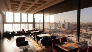 A modern dining area with tables and chairs, large windows offering a city view. - EVA Hotel (Jeddah)