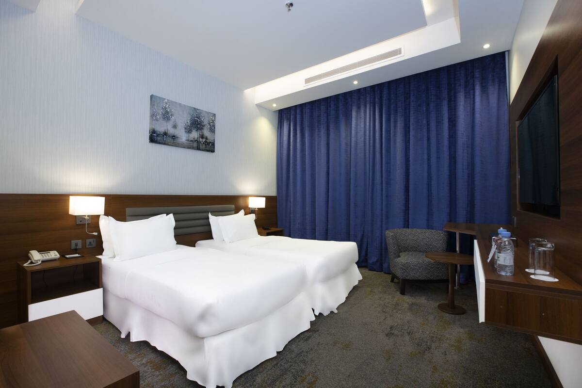 Une chambre d’hôtel avec un grand lit, une chaise, un bureau, un téléphone et un tableau au mur.