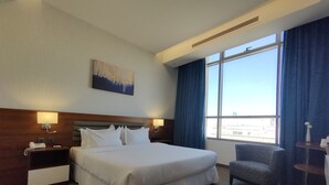 A hotel room with a large bed, two bedside tables, a chair, a painting on the wall, and a large window with curtains. - EVA Hotel (Jeddah)