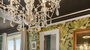 Ein Zimmer mit einem Glastisch, auf dem sich eine Zeitschrift, eine Ananas als Mittelstück und ein Kronleuchter befinden.