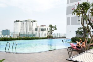 A rooftop pool with a view of high-rise buildings, lounge chairs, and a table.