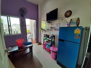 A compact kitchen with a refrigerator, a fan, a TV, and a window.