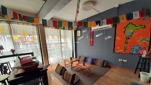 A room with a dining area, a sofa set, a map on the wall, and a window with curtains. - Runa  Runa Guesthouse (Rayong)