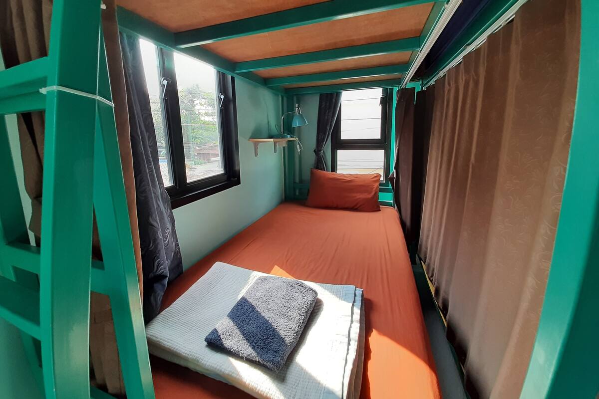 A small, single-bed room with teal walls, a window, and curtains.