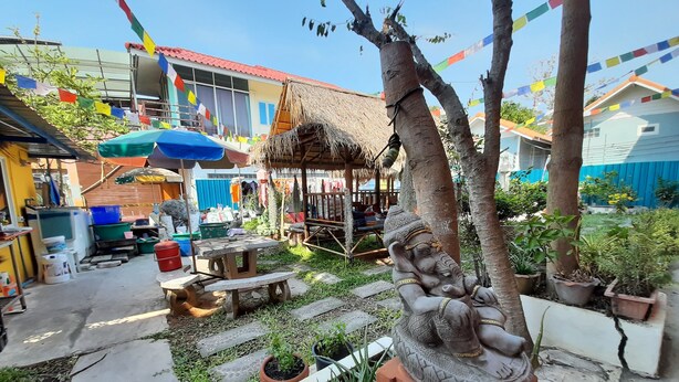 A courtyard with a thatched-roof structure, a statue of an elephant, and colorful prayer flags. - Runa  Runa Guesthouse (Rayong)