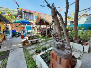 Une cour avec une structure à toit de chaume, une statue d’éléphant et des drapeaux de prières aux couleurs vives.