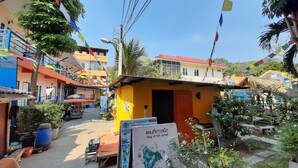 A colorful street scene with a small yellow building, a map sign, and various shops. - Runa  Runa Guesthouse (Rayong)