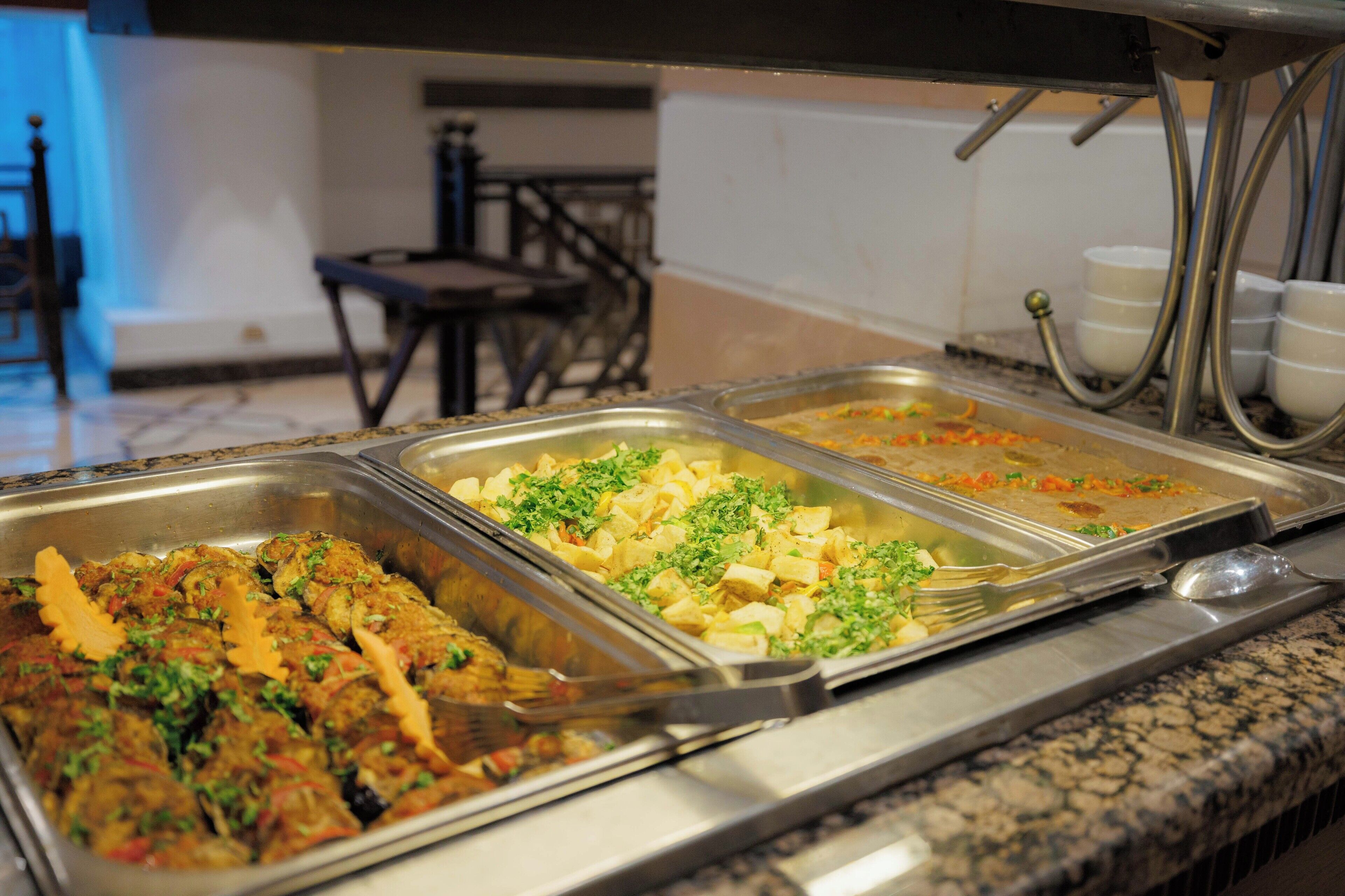 A buffet with various dishes, including what appears to be a meat dish garnished with herbs, a vegetable dish, and a pasta dish.